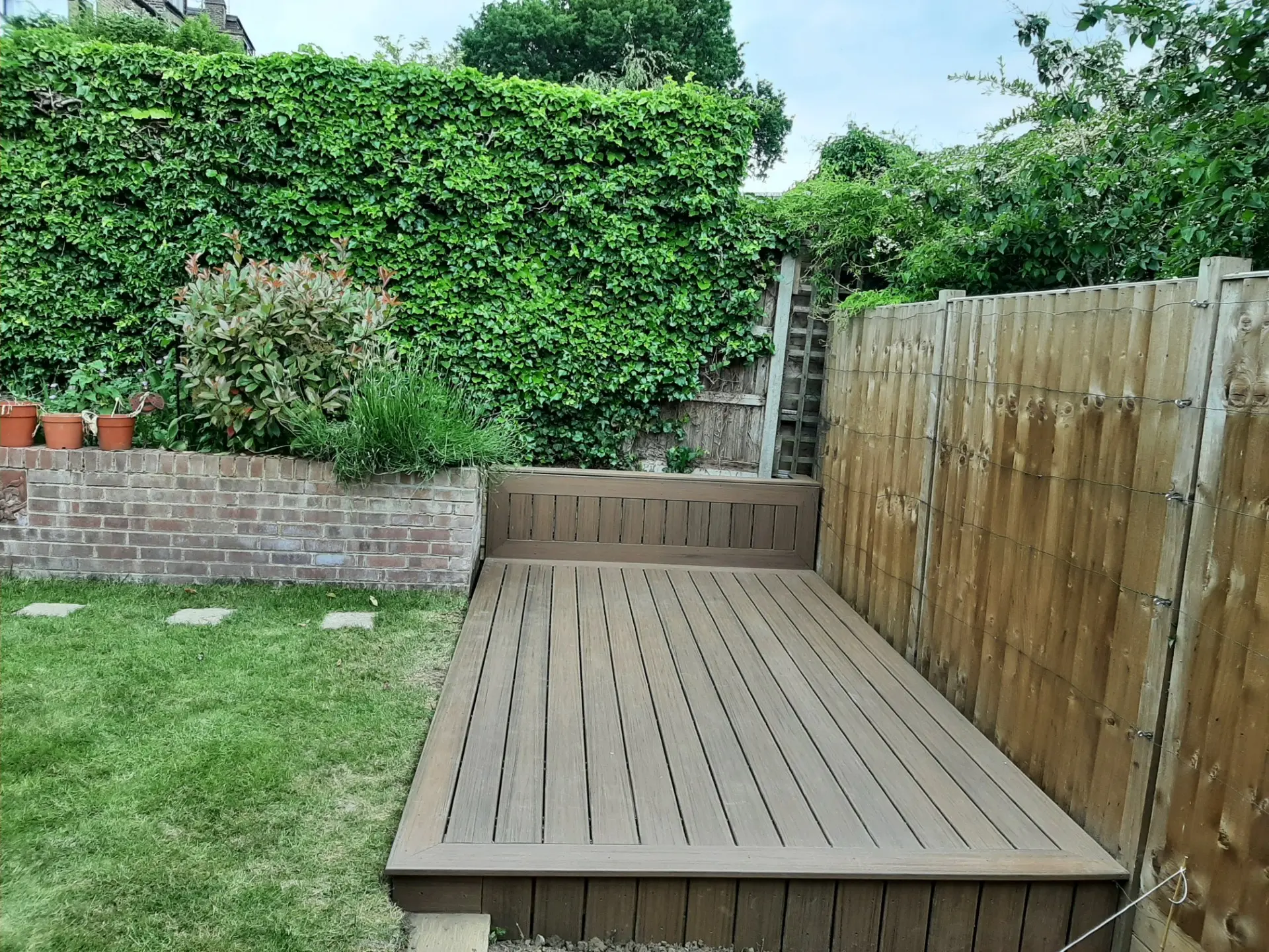 Finished composite deck seen across the lawn with brick retaining wall and ivy hedge behind