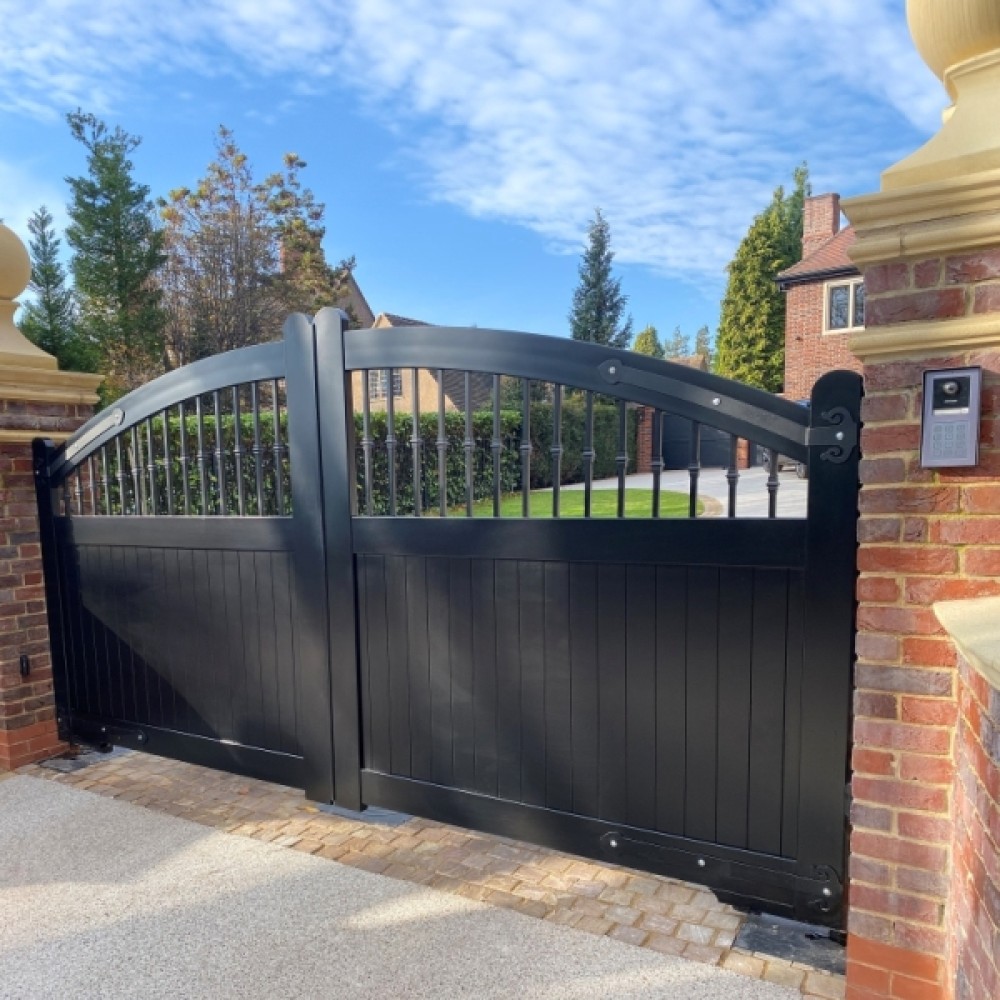 Black aluminium double driveway gates with arched spindle top between brick piers